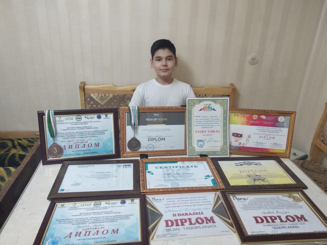 Asadbek with a table full of diplomas and medals, 2020